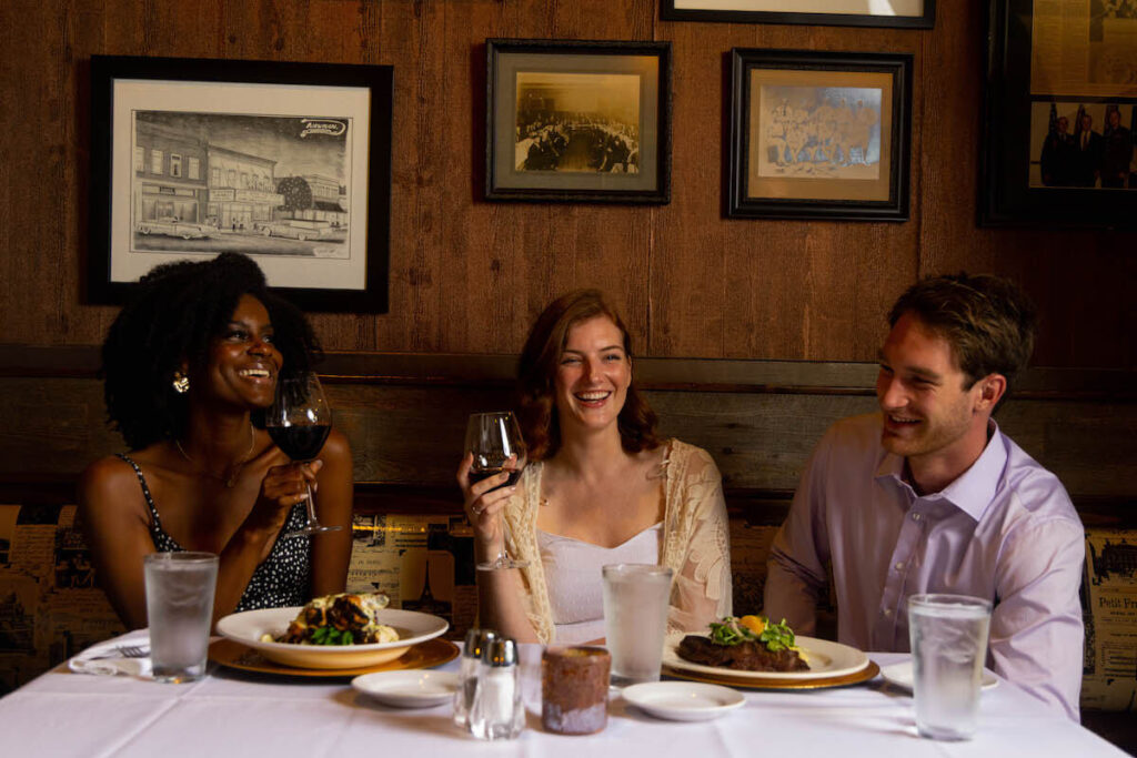 Three friends sharing dinner with steak and wine