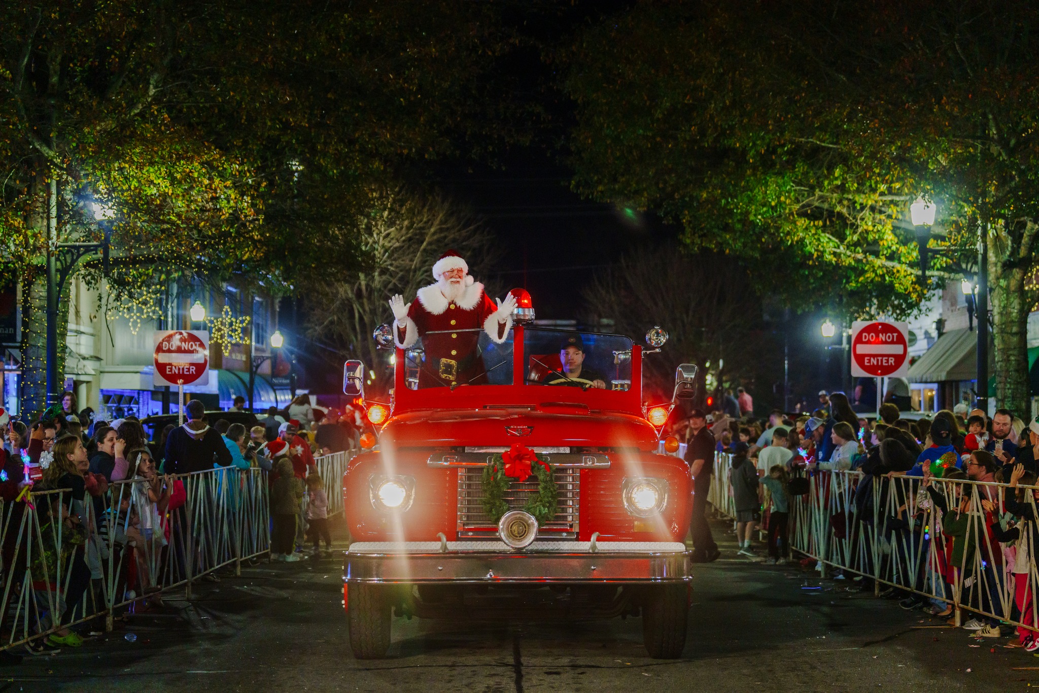 Santa riding down mainstreet in a red firetruck waving to the community.